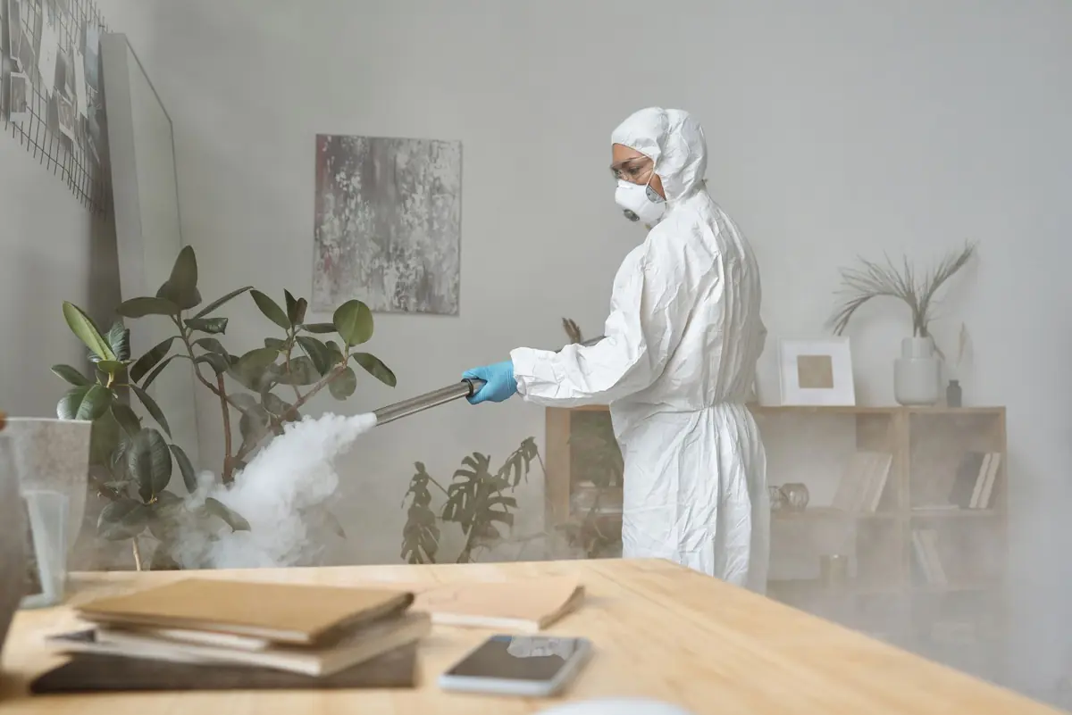 Technician in protective clothing spraying a room